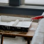 A paint roller and tray with white paint on a wooden table, indicating a renovation work.