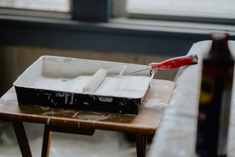 A paint roller and tray with white paint on a wooden table, indicating a renovation work.